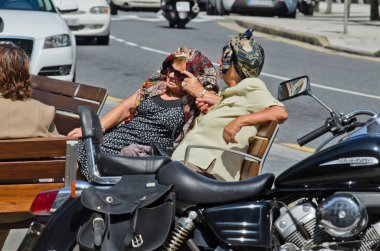 Pontevedra, İspanya - 25 Temmuz 2014: Bir bankta oturan iki kadın, kendilerini başörtüsüyle güneşten korumaya çalışıyorlar.