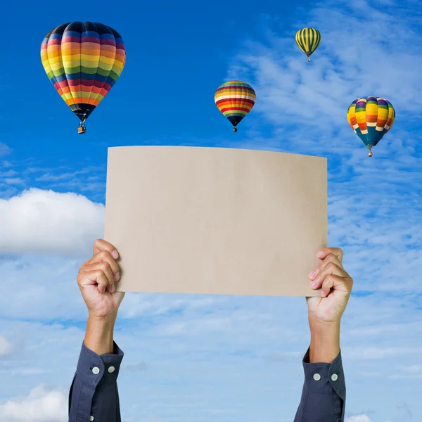 Manos sosteniendo pancarta con globo de aire caliente y fondo de cielo azul — Foto de Stock