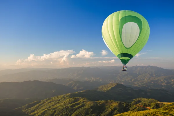 Grüner Heißluftballon über dem Berg bei Sonnenuntergang — Stockfoto