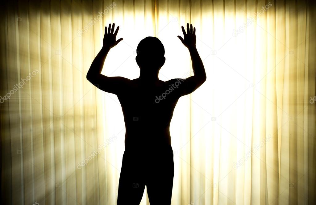 Silhouette of man surrendering with two hands raised in air 