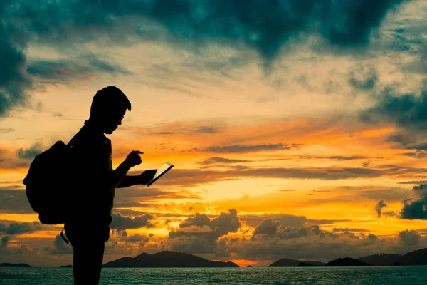 Silueta hombre con tableta digital en las manos al atardecer playa — Foto de Stock
