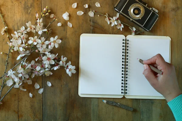 Woman writing on blank notebook next to spring white cherry blossoms tree on vintage wooden table. — Stok fotoğraf