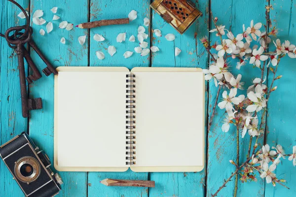 Top view image of spring white cherry blossoms tree, open blank notebook, old camera on blue wooden table — Stockfoto