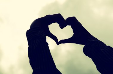 image of hands silhouette in the form of heart against the sunset sky. vintage filtered