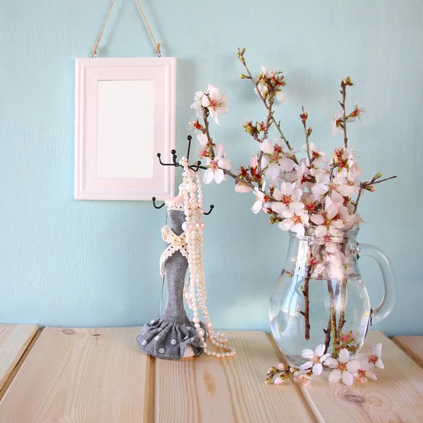 Vintage-Schmuckständer mit Perlenkette, leerer Rahmen neben weißen Frühlingsblumen auf Holztisch — Stockfoto