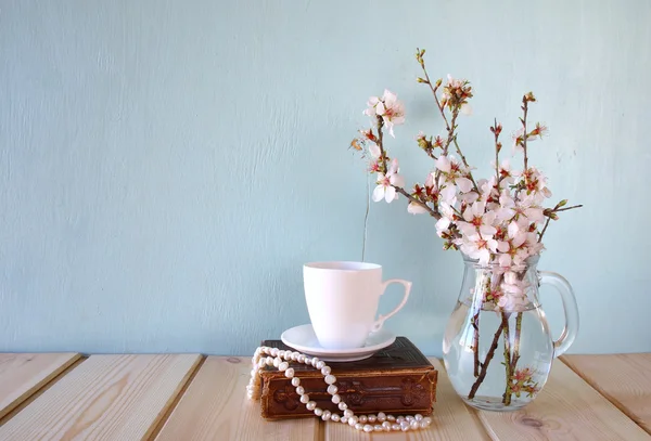 Altes Buch, Perlenkette und Kaffeetasse neben Frühlingsblumen auf hölzerner Textur — Stockfoto