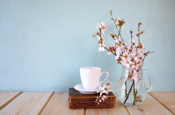 Vanha kirja, kuppi kahvia kevään vieressä valkoisia kukkia puinen rakenne — kuvapankkivalokuva
