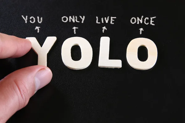 Man hand pointing at the words YOLO you only live once written on black leather background — Zdjęcie stockowe