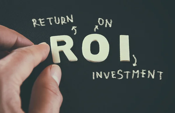 Man hand pointing at the words ROI Return On Investment written on black leather background — Φωτογραφία Αρχείου
