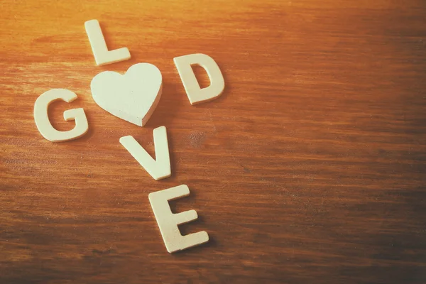 Selective focus photo of The words love is god made with block wooden letters on wooden background. religion concept. vintage filtered and toned — Stock Photo, Image