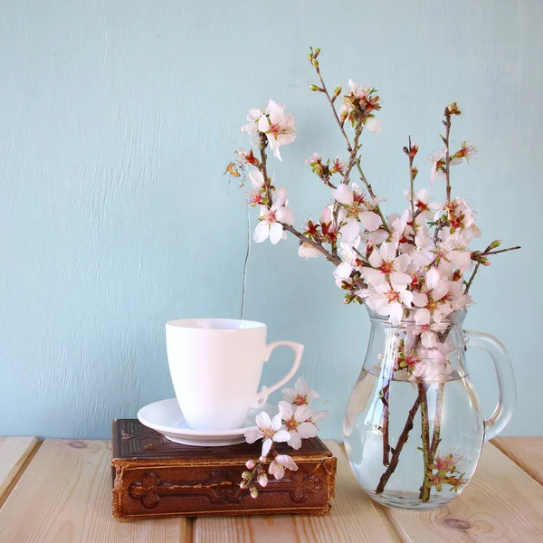 Livro velho, xícara de café ao lado de flores brancas primavera na textura de madeira — Fotografia de Stock