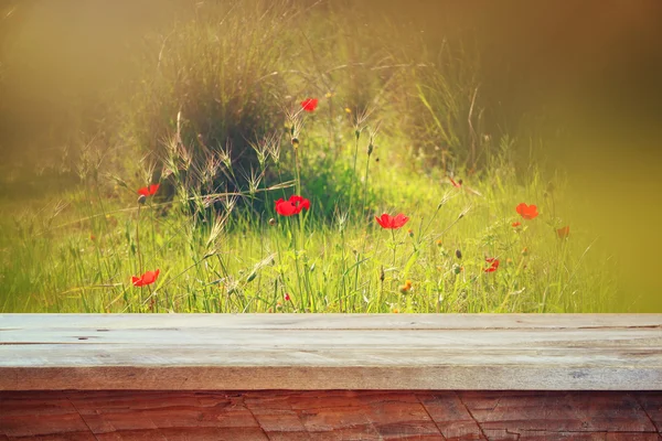 Wooden rustic table in front of red poppies against sky with light burst. vintage filtered image. product display and picnic concept — Stock Fotó