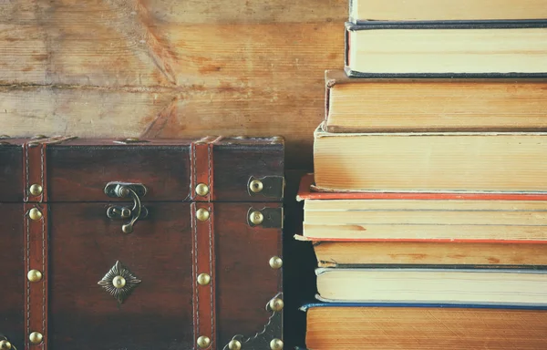 Stack of old books next to antique wooden chest on wooden shelf. vintage filtered and toned — Stockfoto