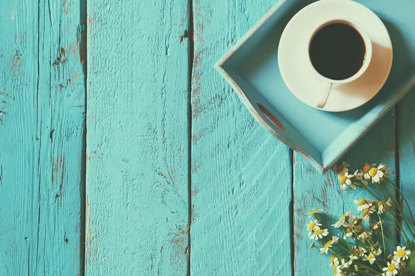 top view image of daisy flowers next to cup of coffee on blue wooden table. vintage filtered and toned