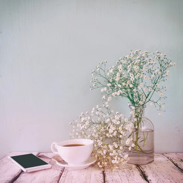 Vintage imagen filtrada y tonificada del teléfono inteligente, taza de café junto a las flores blancas de primavera — Foto de Stock