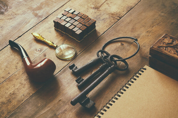 detective concept. Private Detective tools: magnifier glass, old keys, smoking pipe, notebook. top view. vintage filtered image