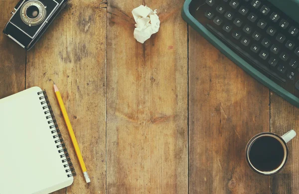 Foto vista superior de la máquina de escribir vintage, cuaderno en blanco, taza de café y cámara vieja en la mesa de madera. imagen filtrada retro —  Fotos de Stock