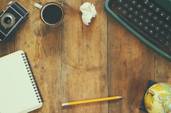 De foto van het bovenaanzicht van vintage typemachine, lege notebook, kopje koffie en oude camera op houten tafel. Retro gefilterde afbeelding — Stockfoto