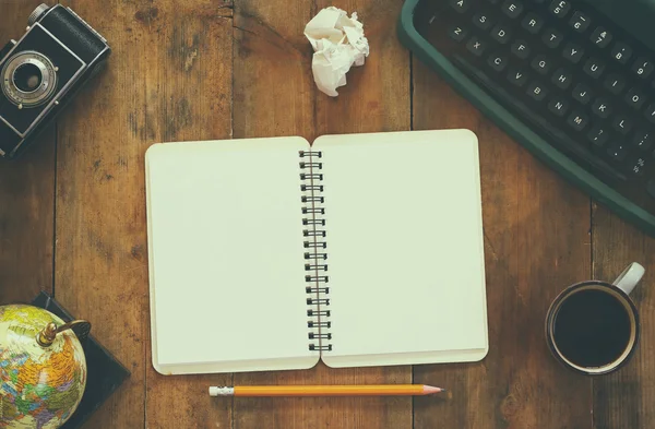 De foto van het bovenaanzicht van vintage typemachine, lege notebook, kopje koffie en oude camera op houten tafel. Retro gefilterde afbeelding — Stockfoto