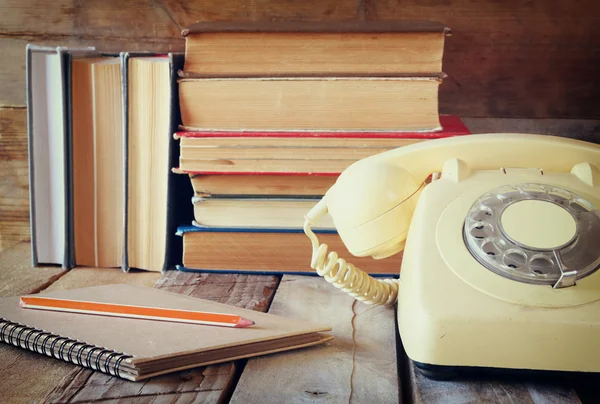 Teléfono de línea vintage, guía telefónica junto a la pila de libros antiguos sobre la mesa de madera. vintage imagen filtrada — Foto de Stock