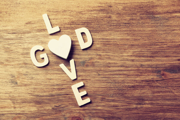 selective focus photo of The words love is god made with block wooden letters on wooden background. religion concept. vintage filtered and toned