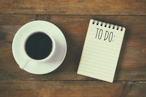 Top view image of blank notebook with the text TO DO, next to cup of coffee on wooden desk. vintage filtered and toned — Stock Photo, Image