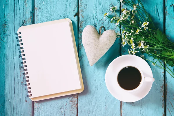 Vintage filtered and toned top view image of daisy flowers, blank notebook and fabric heart next to cup of coffee on blue wooden table. Vintage filtered and toned — стоковое фото