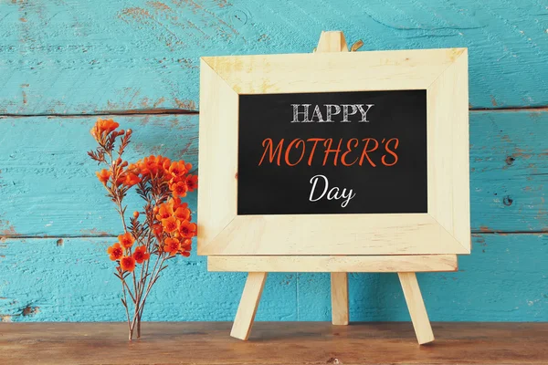 Flowers next to blackboard with phrase: HAPPY MOTHERS DAY, on wooden table. happy mother's day concept — Stock Photo, Image