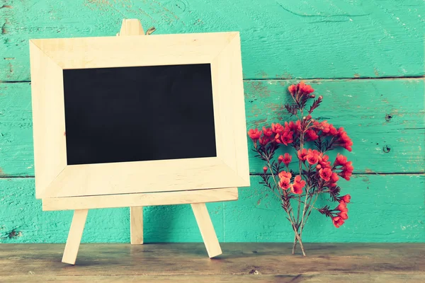 Blank blackboard next to flowers on wooden table — Stock Photo, Image