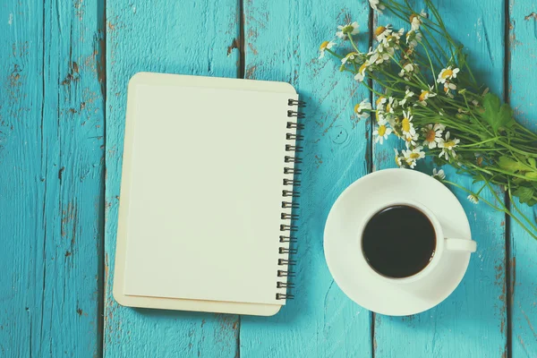 Imagen vista superior de flores de margarita, cuaderno en blanco junto a la taza de café en la mesa de madera azul. vintage filtrado y tonificado —  Fotos de Stock