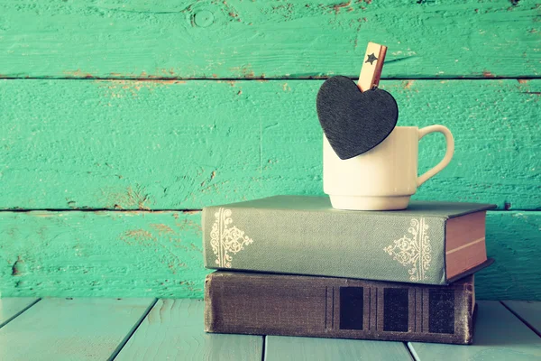 작은 하트 모양의 빈 칠판과 나무 테이블에 오래된 책의 스택 커피 컵. 빈티지 필터링 및 톤 이미지 — 스톡 사진