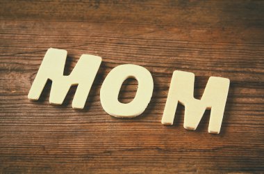 word MOM made with block wooden letters on wooden background. vintage filtered and toned