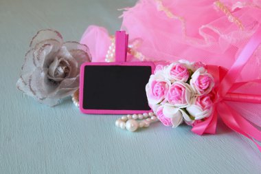 Small girls party outfit: pearls and wand flowers next to small empty chalkboard on wooden table. bridesmaid or fairy costume