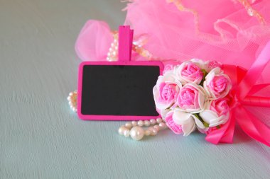 Small girls party outfit: pearls and wand flowers next to small empty chalkboard on wooden table. bridesmaid or fairy costume