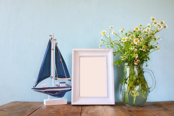 Fresh daisy flowers, blank photo frame and wooden boat on wooden table. vintage filtered — Stockfoto