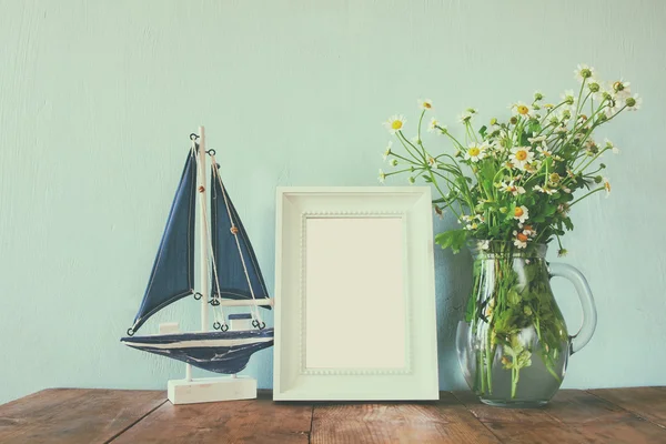 Fresh daisy flowers, blank photo frame and wooden boat on wooden table. vintage filtered — 图库照片