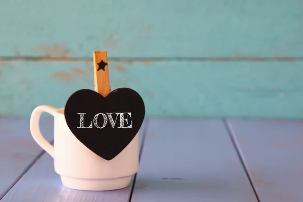 Cup of coffee and little heart shape chalkboard with the word: LOVE. — Stock Photo, Image