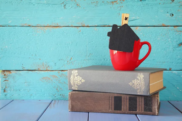 Csésze kávét egy kis ház alakja Chalkboard és a verem a régi könyvek. — Stock Fotó