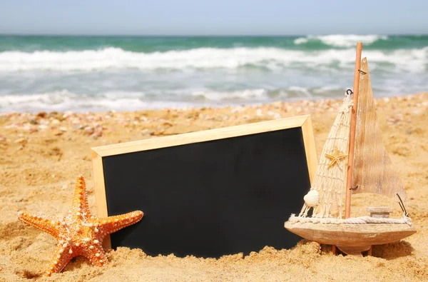 Starfish, sailboat and chalkboard, on sea sand and ocean horizon — Stock Photo, Image
