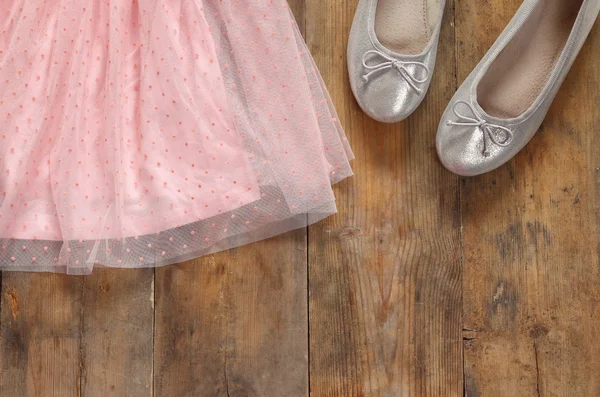 Vintage chiffon girl's dress next to ballet shoes on wooden background. vintage filtered image — Stock Photo, Image