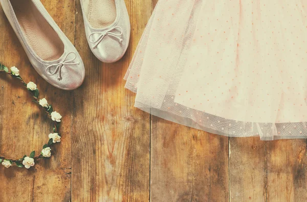 Robe vintage fille en mousseline de soie, tiare florale à côté de chaussures de ballet sur fond en bois. image filtrée vintage — Photo
