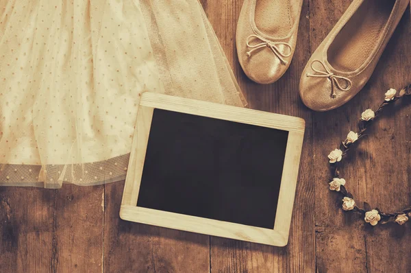Vestido da menina chiffon vintage, tiara floral ao lado de sapatos de balé e quadro preto em branco no fundo de madeira. imagem filtrada vintage, foto estilo sépia — Fotografia de Stock