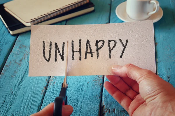 Man hand holding card with the text unhappy, cutting the word un so it written happy. retro style image — Stock Photo, Image