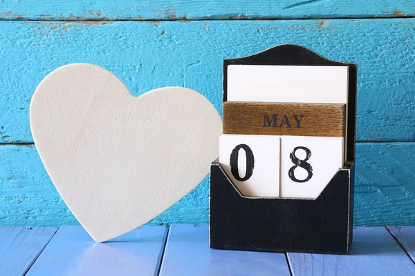 Flores junto a tabla en blanco en forma de corazón en la mesa de madera. concepto del día de la madre feliz — Foto de Stock