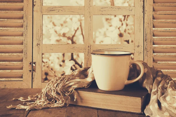 Romantische Szene einer Tasse Kaffee neben einem alten Buch vor dem Blick auf die Landschaft vor dem alten rustikalen Fenster. Vintage gefiltertes Bild — Stockfoto