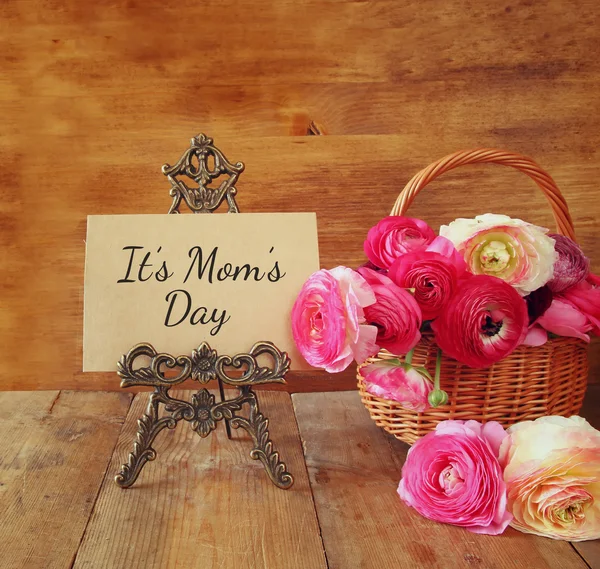 Розовые цветы в корзине рядом с карточкой, на деревянном столе. happy mother 's day concept — стоковое фото
