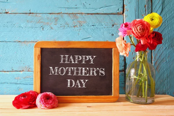 Flowers next to blackboard, on wooden table. happy mother's day concept — Stock Photo, Image