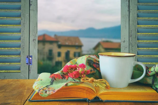 Romántica escena de taza de café junto al viejo libro frente a la vista del campo fuera de la vieja ventana rústica. vintage imagen filtrada y tonificada — Foto de Stock