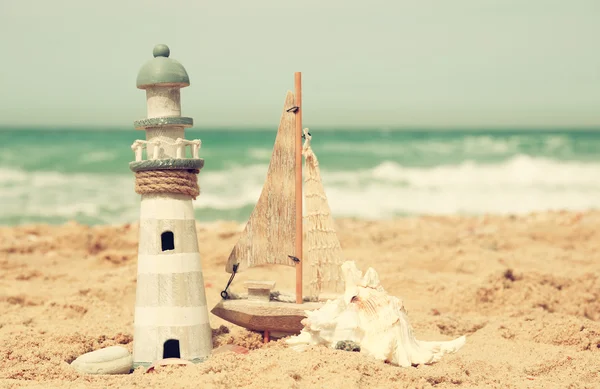 Lighthouse, sailboat on sea sand and ocean horizon. — Stock Photo, Image