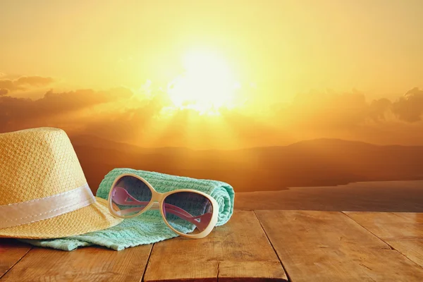 Fedora hoed en zonnebril over houten tafel en zonsondergang — Stockfoto